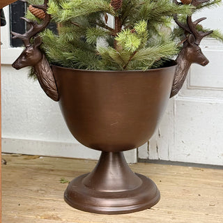 Bronze stag pedestal bowl used as festive planter holding small evergreen tree on cozy Christmas porch