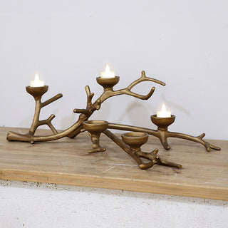 Cast iron branch tealight holder with three lit tealights displayed on rustic wood shelf