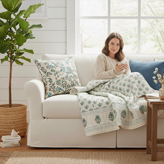  Woman relaxing on white couch with hand block print cotton throw featuring blue-green botanical motifs