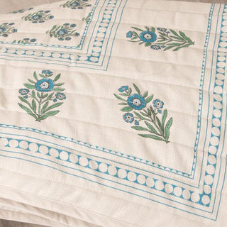 Close-up detail of hand block print botanical motifs showing blue-green flowers and decorative border on natural cotton