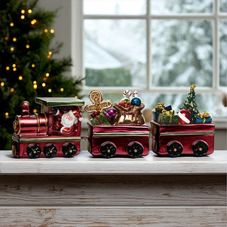 Red metallic resin Christmas train set with Santa in engine, toy bag with ornaments in middle car, and Christmas tree with presents in caboose displayed on white mantel with snowy window background