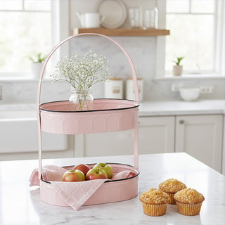  Blush pink two-tier metal serving tray with scalloped edges displayed on white kitchen counter with apples and muffins