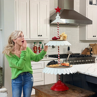 Woman in green sweater admiring a tall three-tiered holiday serving stand with red and white details in a modern kitchen