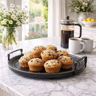 Distressed black round serving tray with blueberry muffins on marble countertop with French press coffee