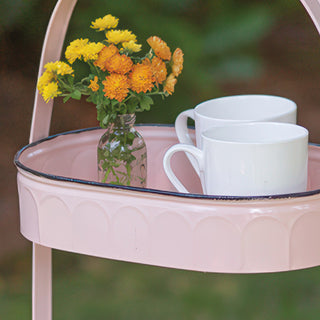 Close-up of scalloped edge detail on blush pink metal serving tray top tier with white coffee mugs and flowers