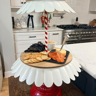 Charcuterie spread with crackers, cheese, pepperoni, grapes, and nuts on the bottom tier of red and white serving stand