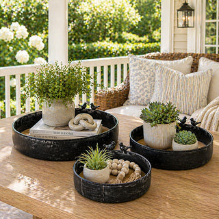Set of three black metal trays with wood bases and bird accents on outdoor table
