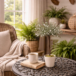 Faux white bloom topiary tree in cream ceramic pot with moss topper on decorative metal table