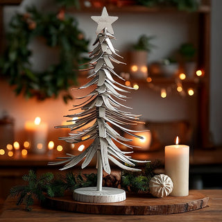 Rustic distressed white metal Christmas tree with star topper displayed on wooden surface with candles and pine branches creating farmhouse holiday ambiance