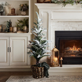 4-foot flocked farmhouse Christmas tree with burlap base next to fireplace with lanterns and woven basket in cozy living room