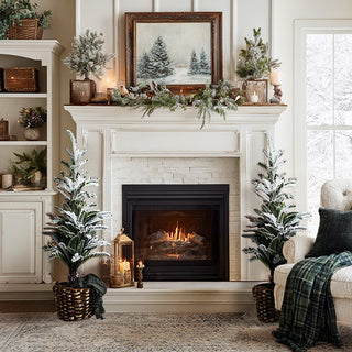 Pair of flocked Christmas trees flanking fireplace mantel with winter woodland decor - farmhouse holiday styling with burlap bases