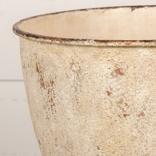 Close-up detail of distressed cream metal urn opening rim showing textured weathered finish and raw metal edge detail