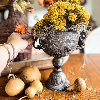 Decorative black urn with dried flowers on a wooden surface