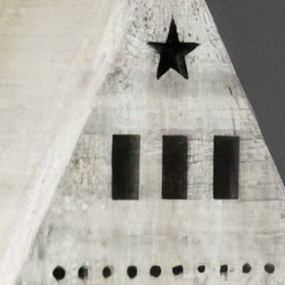 Close-up of distressed white wooden village house roof peak showing black metal star cutout and punched dot detailing